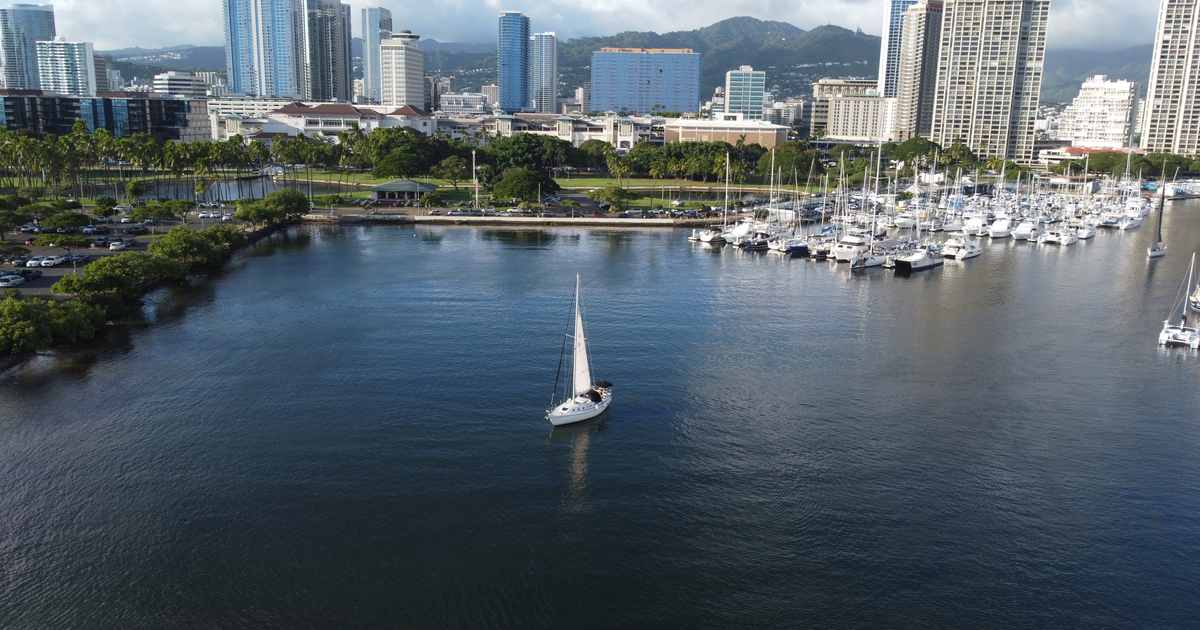 Sailboat motoring out of Ala Wai Boat Harbor with the Honolulu skyline behind, Oahu, Hawaii