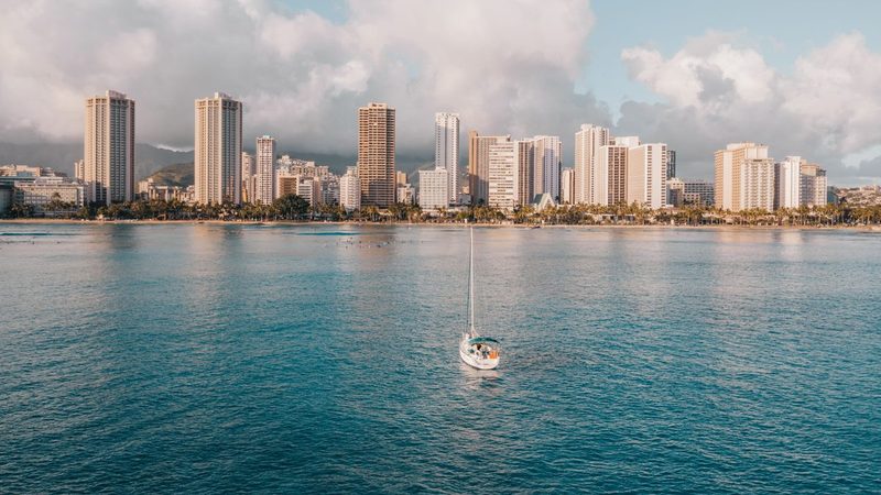 A sailboat under way on turquoise water in front of the Waikiki skyline, Oahu, Hawaii
