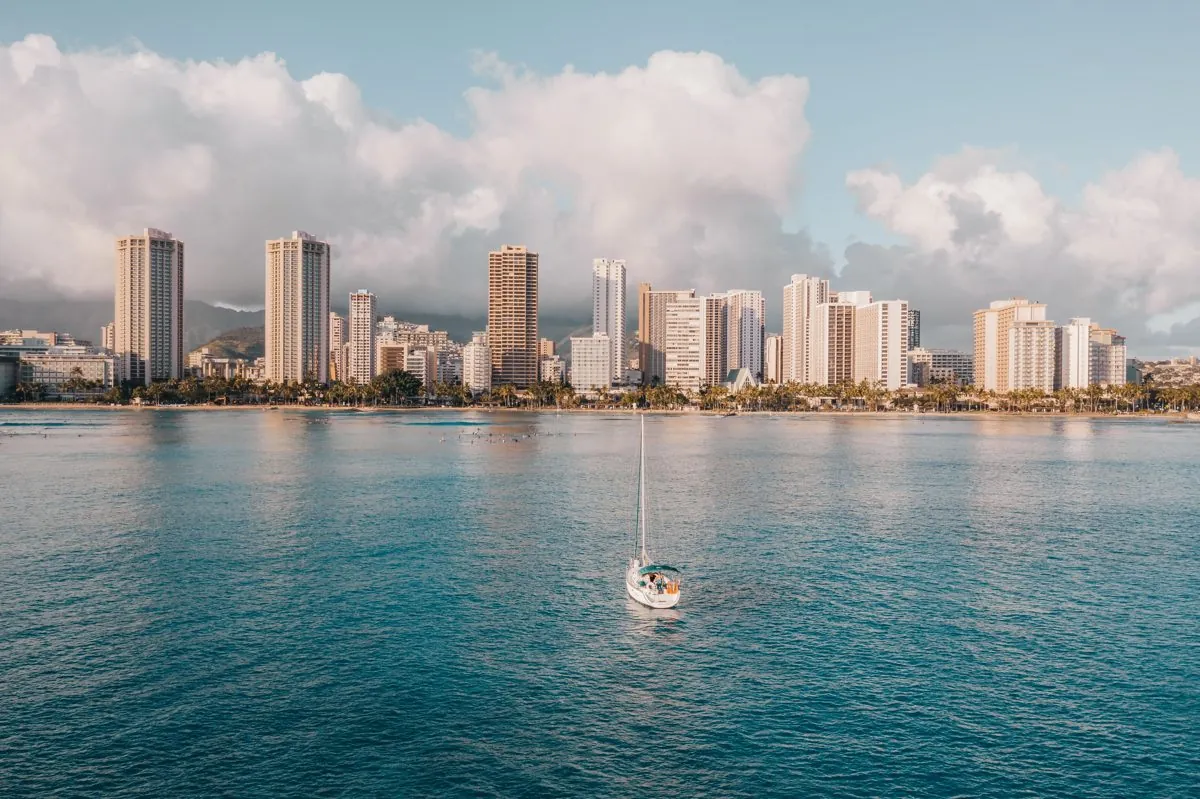 A sailboat under way on turquoise water in front of the Waikiki high-rise skyline and mountains, Oahu, Hawaii