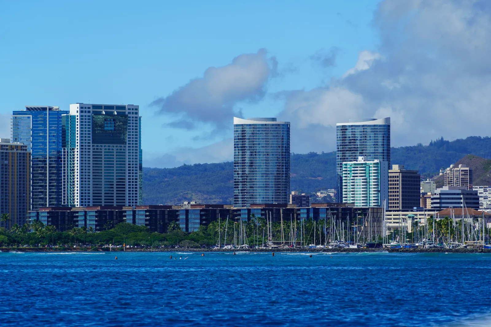 Honolulu skyline rising above an Oahu harbor full of moored sailboat masts, where Hawaii boats are registered and titled