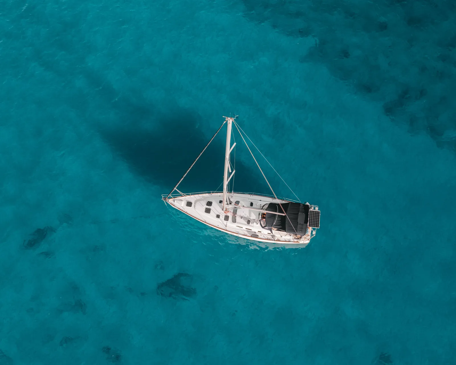 Aerial overhead view of a white sailboat anchored on clear turquoise Hawaii water, the kind of used boat a buyer would survey and sea-trial