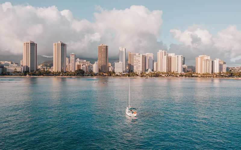 A sailboat anchored on calm blue water off Waikiki with the Honolulu skyline behind, Oahu