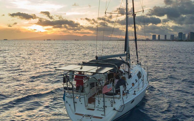 Aerial drone view of the Hunter 45 sailboat Praha off Honolulu at sunset with the Waikiki skyline behind