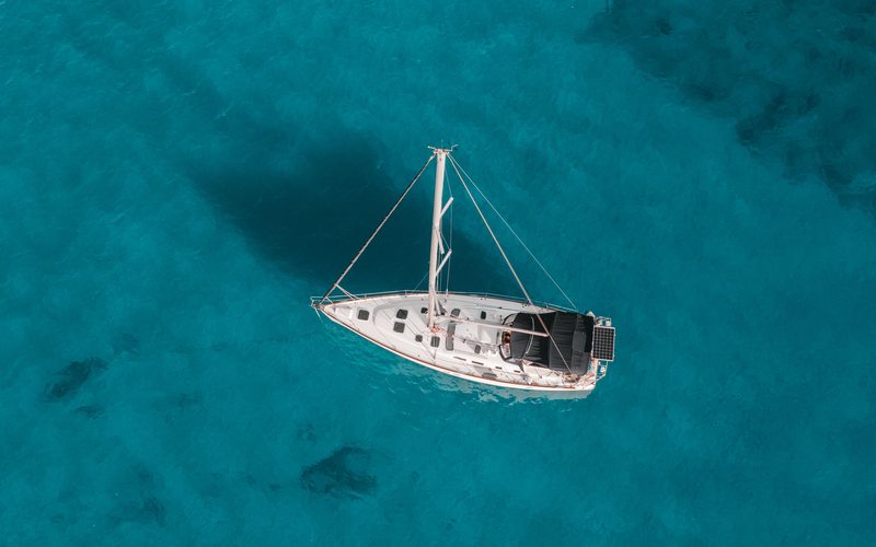 Aerial view of a white sailboat anchored over clear turquoise water off Oahu