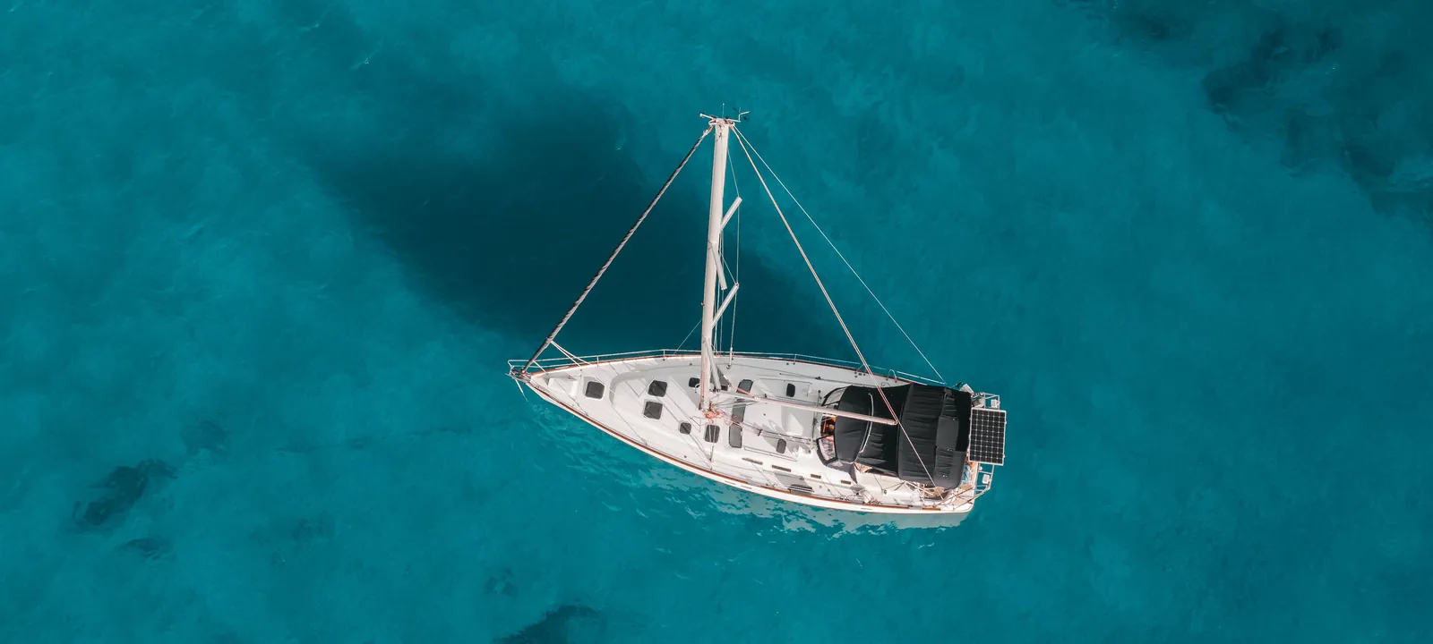 Aerial view of a white sailboat anchored over clear turquoise Hawaiian water off Oahu
